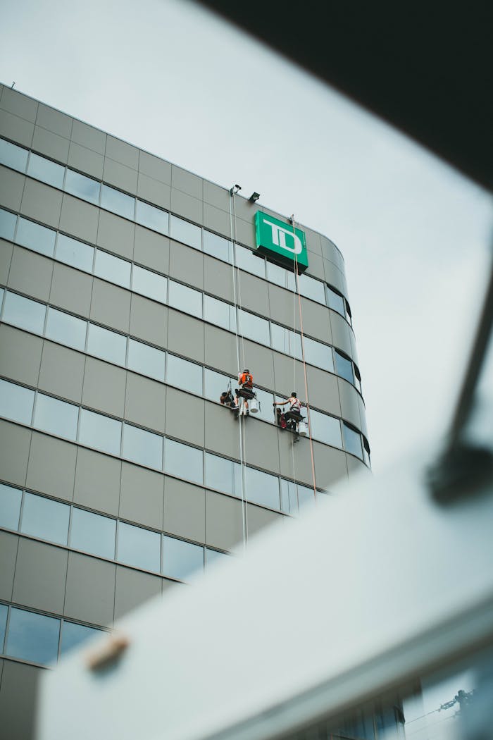 Two professional window cleaners working on a skyscraper with a corporate logo.